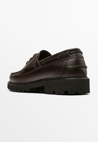 Bruine leren bootschoen met een gladde afwerking, dikke zwarte rubberen zool, vetersluiting en gedetailleerde stiksels langs de randen.