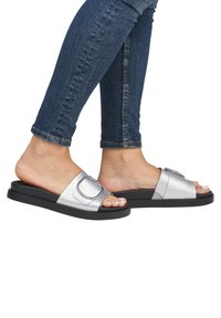 Sandales à glissière argentées avec une sangle texturée et un accent à double boucle, dotées d'une semelle en caoutchouc noire et d'un design ouvert au niveau des orteils.