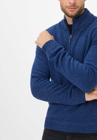 Maglione azzurro in maglia con collo alto, chiusura con zip e polsini a coste. Presenta un tessuto strutturato e un design aderente.