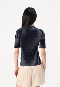 Camică cu mânecă scurtă, cu dungi albastre și albe, cu guler rotund, fabricată dintr-un material ușor, combinată cu pantaloni scurți bej. Design curat și casual.
