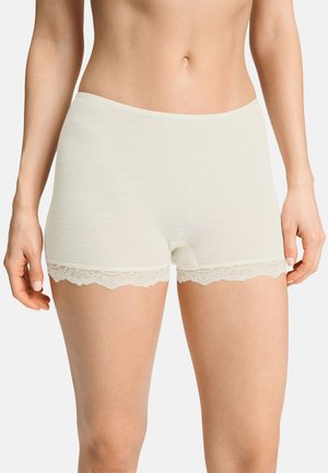 Mujer con pantalones cortos acanalados de color crema con ribete de encaje en las aperturas de las piernas, mostrada desde la mitad del torso hasta la mitad del muslo.