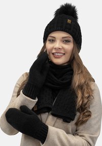 Sort strikket vinterhat med pom-pom, matchende sort tørklæde og vanter. Struktureret mønster med subtilt mærketag.