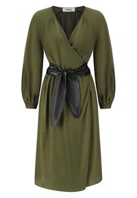 Robe longue à manches longues de couleur vert olive avec un décolleté en V, des poignets froncés et une large ceinture en cuir noir nouée à la taille.