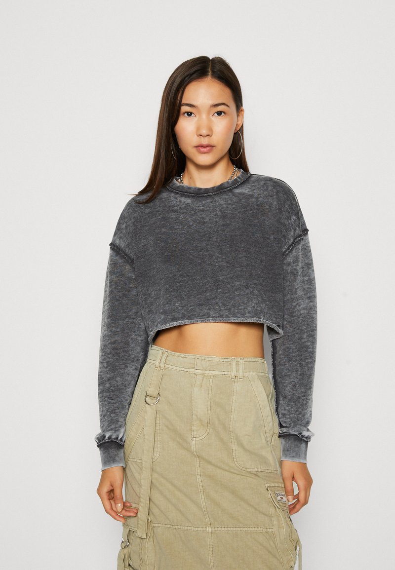 Felpa grigia a coste, corta, con maniche lunghe e bordi grezzi, abbinata a una gonna cargo color khaki con texture e tasche laterali.