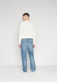 Camisa blanca de manga larga combinada con jeans de pierna recta azul claro, con bolsillos traseros y un corte holgado, llevada con zapatillas blancas.