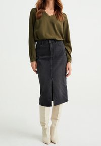 Olivgrön långärmad blus med spetsdetaljer, i kombination med en mörkgrå denim midi-kjol med hög midja och en framkant.