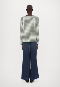 Pruhovaný dlouhý rukáv v zelené a bílé barvě spárovaný s širokými modrými džíny. Textura je hladká a střih je uvolněný.