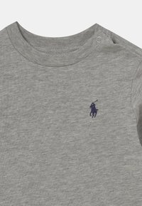 Gray cotton t-shirt with a soft texture, featuring a round neckline and snap buttons on one shoulder. A small navy logo is on the chest.