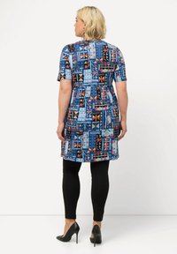 Kuviollinen mekko lyhyillä hihoilla, jossa on sininen, musta, punainen ja akvaariodesign. Yhdistetty mustien legginsien ja korkokenkien kanssa.