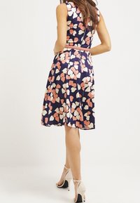 Kleid mit Blumenmuster in Marineblau mit rosa und cremefarbenen Herzformen. Ärmellos, tailliert, mit ausgestelltem Rock und einem sichtbaren Reißverschluss auf der Rückseite.