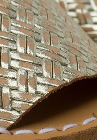 Goudgeweven textuurleer met een beige achterkant, voorzien van een gladde afwerking en zichtbare stiksels langs de rand.