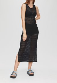 Musta neulemekko, jossa on hihaton malli, avoin neuloskuvio ja polvipituus. Yhdistetty sinisiin sandaaleihin, joissa on paksu pohja.