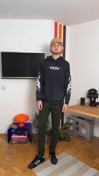 Μαύρη φούτζα με λευκό σχέδιο φλόγας στα μανίκια, συνδυασμένη με ελαιοπράσινα παντελόνια και μαύρα αθλητικά παπούτσια. Χαλαρό στυλ με άνετη εφαρμογή.