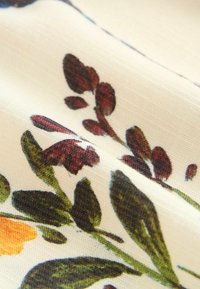 Tessuto floreale con uno sfondo crema e motivi botanici multicolori nelle tonalità di verde, rosso e arancione. Texture liscia.