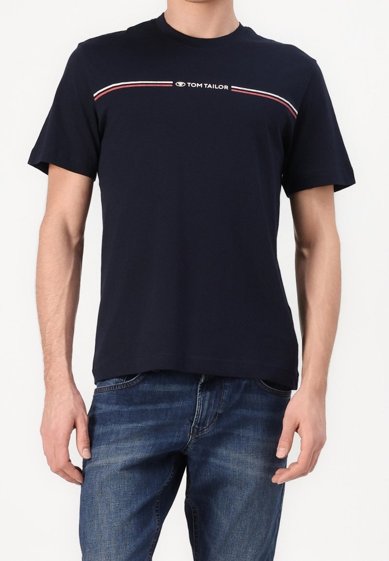 T-shirt en coton bleu marine à manches courtes, avec une rayure horizontale blanche et rouge et le logo "TOM TAILOR" sur la poitrine.