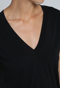 Zwarte V-hals top met korte mouwen, gemaakt van zachte stof. Heeft subtiele stikdetails langs de halslijn en schouders.