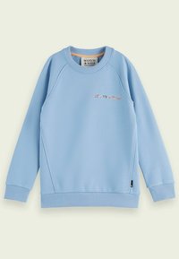 Felpa azzurra chiara in morbido cotone, con polsini e orlo a coste, su cui sono ricamate in lettere colorate le parole "SCOTCH & SODA" sul davanti.