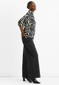Long-sleeve, black and cream zebra-patterned blouse paired with high-waisted, wide-leg black jeans and black heeled boots.