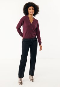 Burgundský cardigan s výstřihem do V, se šesti knoflíky vpředu a žebrovanými manžetami, nošený s černými rovnými kalhotami a metalickými botami na podpatku.