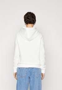 Sudadera blanca con capucha, de corte relajado, textura suave y puños acanalados, combinada con unos jeans de tiro alto en azul claro.