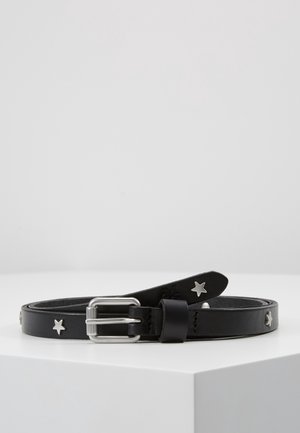 Ceinture en cuir noir avec des clous étoiles argentés et une boucle rectangulaire argentée, enroulée sur une surface blanche sur fond gris uni.