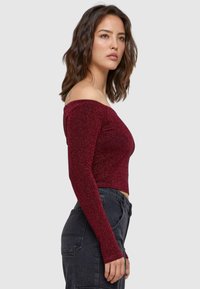 Burgundi off-the-shoulder felső hosszú ujjal, csillogó anyagból készült, rövidített fazonú és testhezálló sziluettel.
