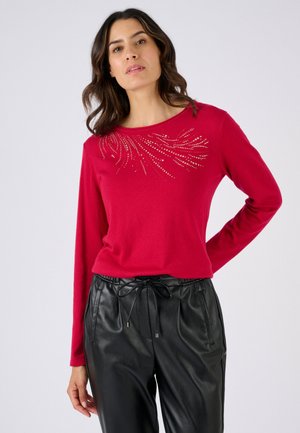 Red long-sleeve top featuring a round neckline and embellished with a beaded design across the chest, paired with black, drawstring waist pants.