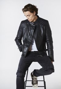 Svart läderbikerjacka med kviltade axlar, dragkedja fram och vass design. Bärs med slitna svarta jeans och mörka sneakers.