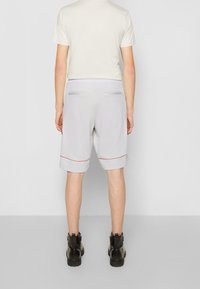 Pantaloni sportivi grigi con piping rosso, vita elasticizzata e due tasche posteriori. Indossati con una maglietta chiara e stivali neri.
