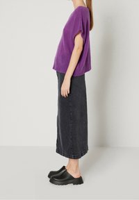 Lila stickad t-shirt med kort ärm i kombination med en svart denim maxikjol och svarta slip-on klotsskottar, som visar en mjuk textur och en avslappnad silhuett.