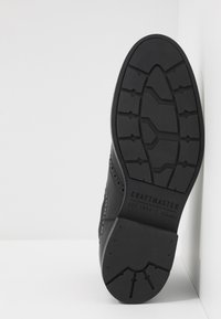Zwarte leren schoenonderkant met ingewikkeld profiel, met de ingedrukte merknaam "CRAFTMASTER" in verhoogde letters.