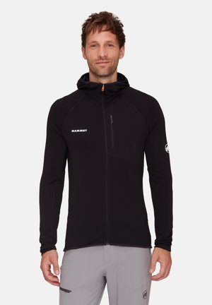 Giubbotto in pile nero con cappuccio, tasca sul petto con zip, dettagli riflettenti e materiale testurizzato. Presenta un tirazip arancione a contrasto.
