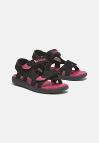 Musta ja vaaleanpunainen Timberland-sandaalit tarranauhakiinnityksellä, kumipohjalla, avonaisella varvasmuotoilulla ja tekstuuripohjalla, joka tarjoaa pitoa.