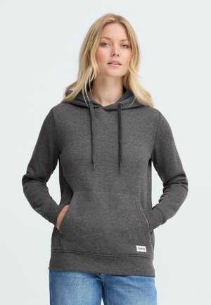 Mørkegrå hettegenser med kengurulomme, snorer og ribbestrikkede mansjetter, brukt over blå jeans, med en liten logoetikett.