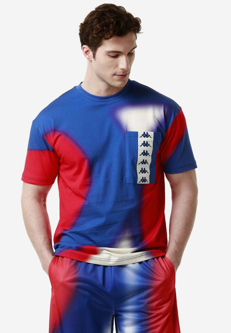 Camiseta colorida de manga corta con un diseño de degradado en azul, rojo y blanco, con un bolsillo delantero que muestra los logotipos de la marca.
