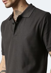 Dunkelgraues Poloshirt aus strukturiertem Gewebe, mit klassischem Kragen, Drei-Knopf-Leiste und kurzen Ärmeln.