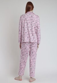 Conjunto de pijama rosa hecho de tela suave, que presenta un diseño estampado con figuras de dibujos animados y texto escrito a mano. Mangas largas y pantalones de corte recto.