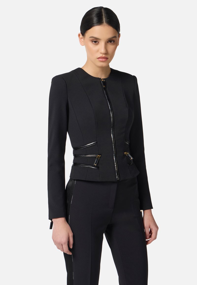 Chaqueta negra entallada con mangas largas, cremallera frontal y acentos con cremallera en la cintura. Tejido suave con elementos de diseño estructurados.