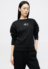 Melnas sporta džemperis ar apaļu kakla izgriezumu un garām piedurknēm, ar balta krāsā drukātu logotipu "ACX ARMANI EXCHANGE" krūšu daļā. Gluda tekstūra.