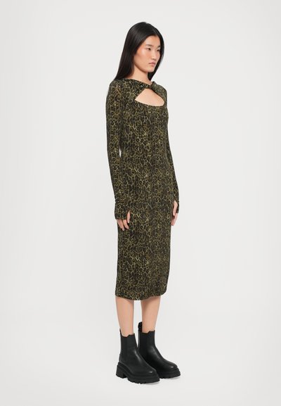 Robe ajustée à manches longues en imprimé léopard vert et noir avec un détail découpé au niveau du col, accompagnée de bottines noires à la cheville.