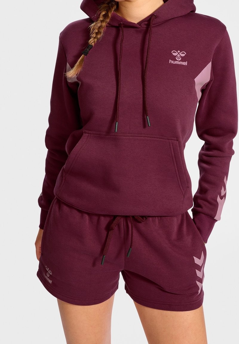 Sudadera burdeos con un bolsillo frontal y cordón, combinada con shorts a juego que presentan un logo y un diseño de chevron lateral en rosa claro.