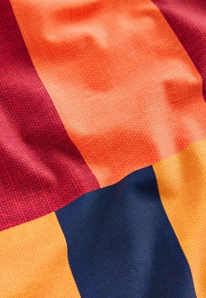 Textiel met grote blokken in rood, oranje, geel en donkerblauw in een textuurstof, met een roosterachtige patroon.