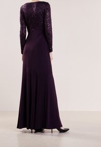 Lange paarse jurk met een met sequins bezette kant bodice en een vloeiende rok, met lange mouwen en een gladde textuur. De jurk heeft een lichte sleep.