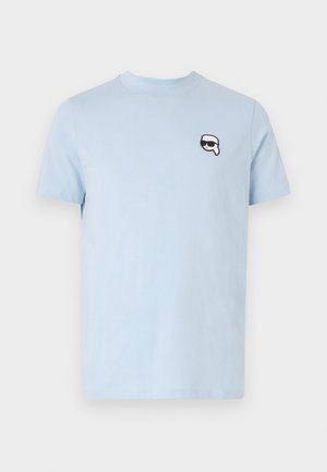 Hellblaues Baumwoll-T-Shirt mit Rundhalsausschnitt und kurzen Ärmeln. Beinhaltet ein kleines schwarz-weißes Grafik-Patch auf der linken Brust.