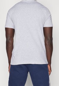 Grå, kortärmad t-shirt i bomullsblandning. Har rund halsringning och en avslappnad passform, bärs tillsammans med marinblå byxor.