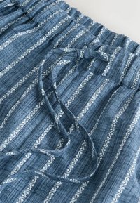 Tissu bleu avec des rayures blanches horizontales et de petits motifs en losange, doté d'une taille élastique et d'un cordon de serrage. Léger et texturé.