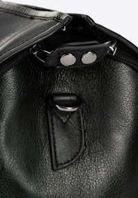 Interior de una bolsa de cuero negro con cierre de cremallera, con herrajes plateados y un detalle de botón a presión cerca de la abertura. Textura suave.