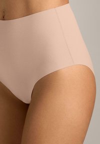 Slip beige a vita alta realizzato in tessuto liscio ed elasticizzato, caratterizzato da un design senza cuciture, taglio a vita media e dettagli di cucitura minimali.