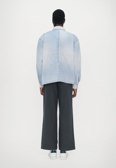 Lys blå denim oversized jakke med en lett falmet overflate, kombinert med mørke vide bukser og hvite sneakers med grønne detaljer.