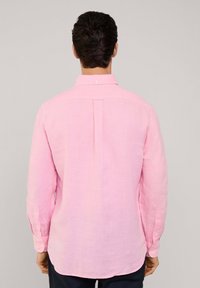 Camisa de lino rosa de manga larga con pliegue en la espalda y cuello de botón. Presenta puños abotonados y un dobladillo curvado. Textura suave.